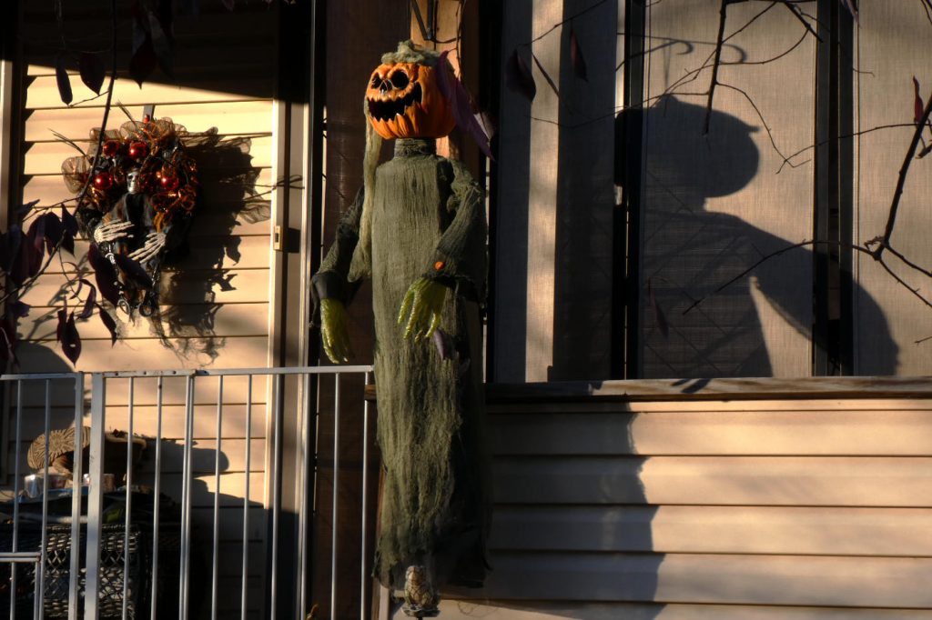 Carved pumpkin head hanging with a ghost effigy on a shadowy wooden porch