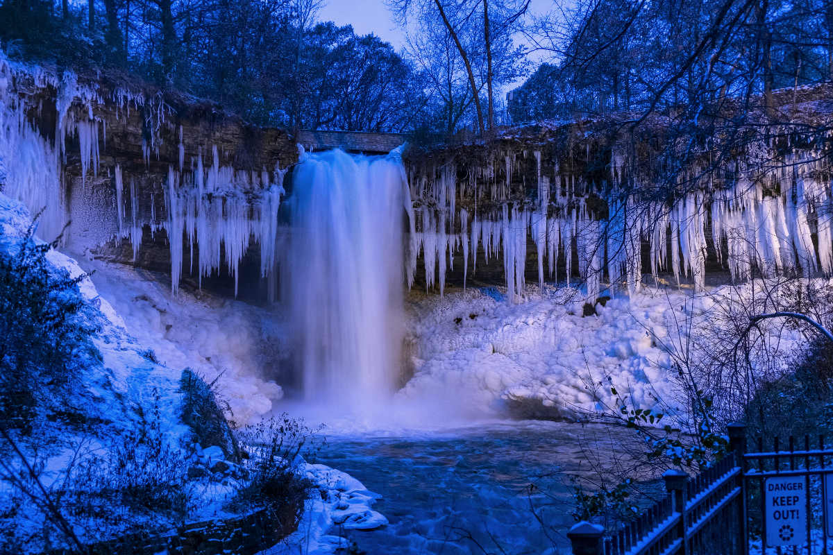 wide view of running waterfall with surrounding icy walls in mostly blue shadow with some sunlight on the right side