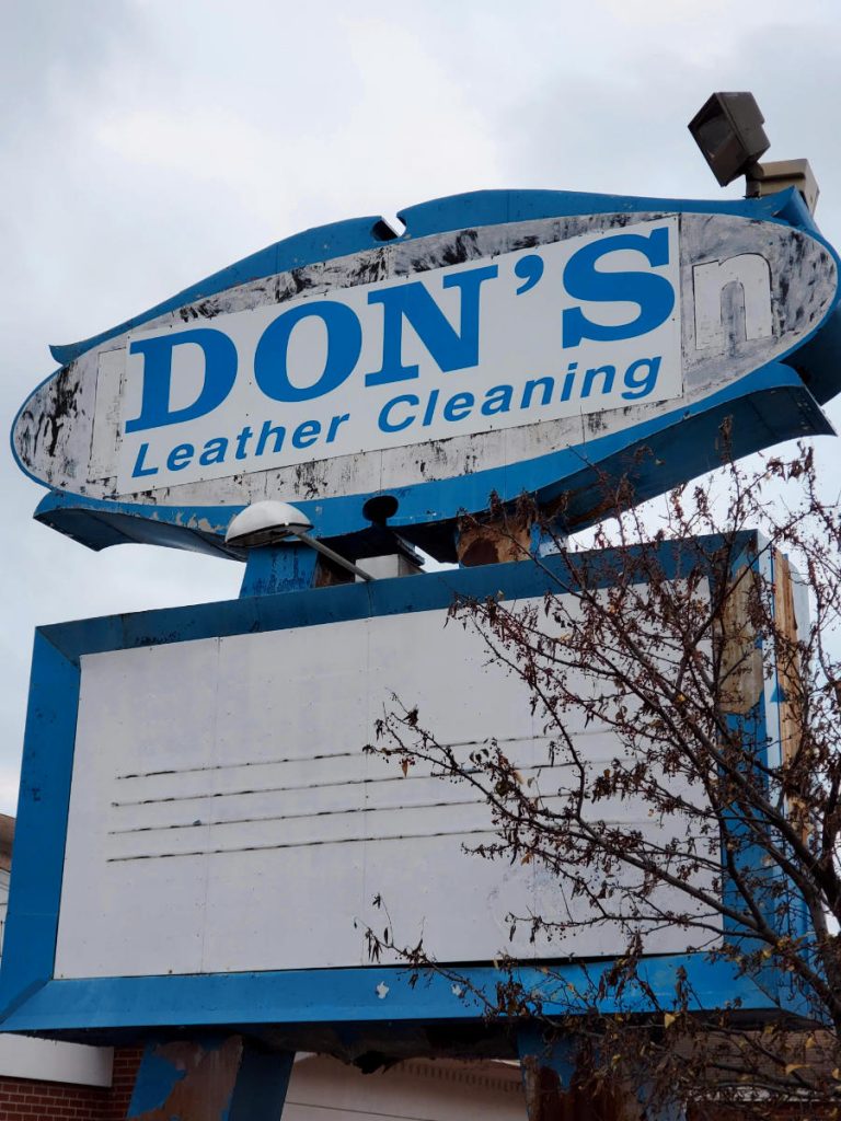 White sign with blue lettering that reads DON'S Leather Cleaning