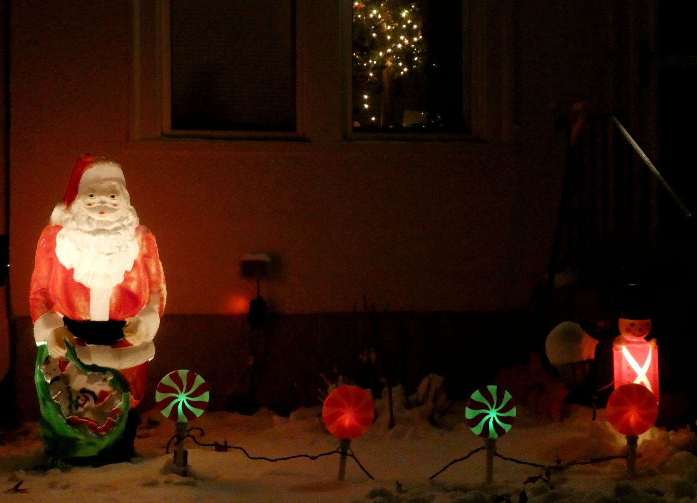 Lit-up santa yard statue with green and yellow candelsticks and a smaller nutcracker statue