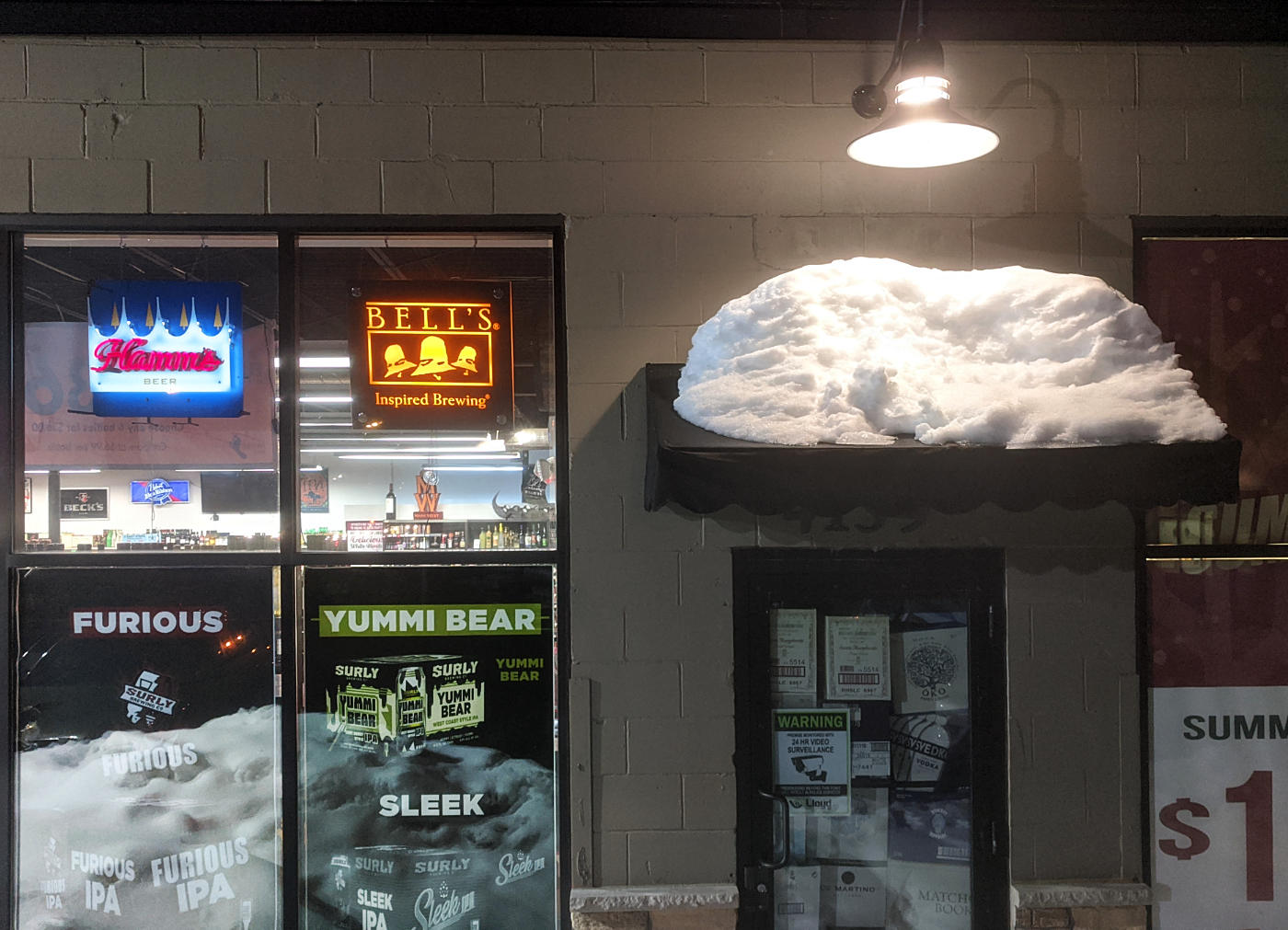 Mound of snow atop a doorway overhang next to a store window with neon lights