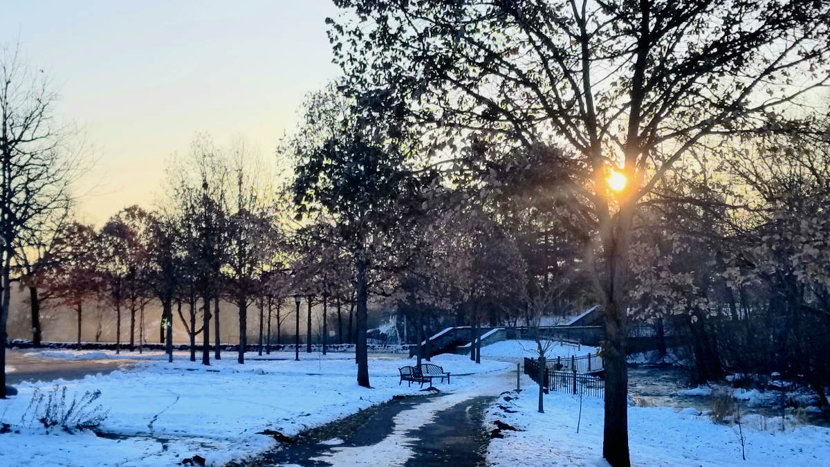 Sunrise scene in snowy park with benches, stone walls and stairway in backbround