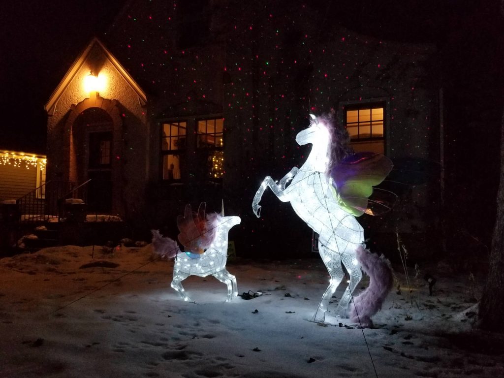 Two lit-up unicorn statues at night in a front yard