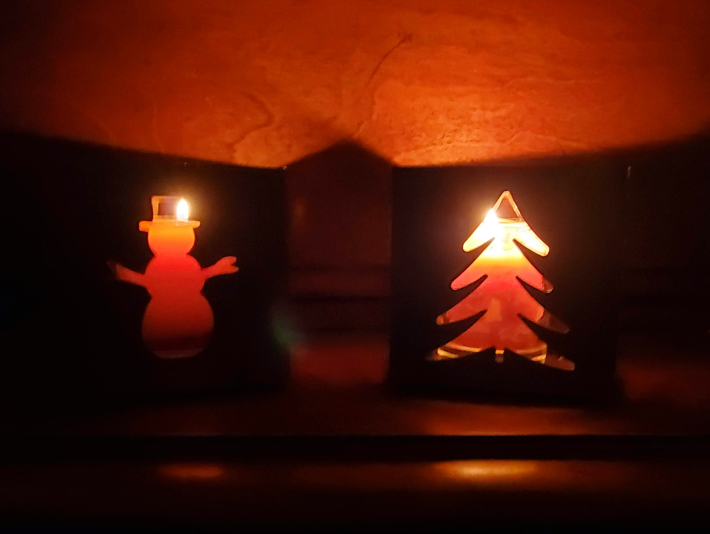 cutouts of a snowman and evergreen tree glow with orange-yellow light from candle flames
