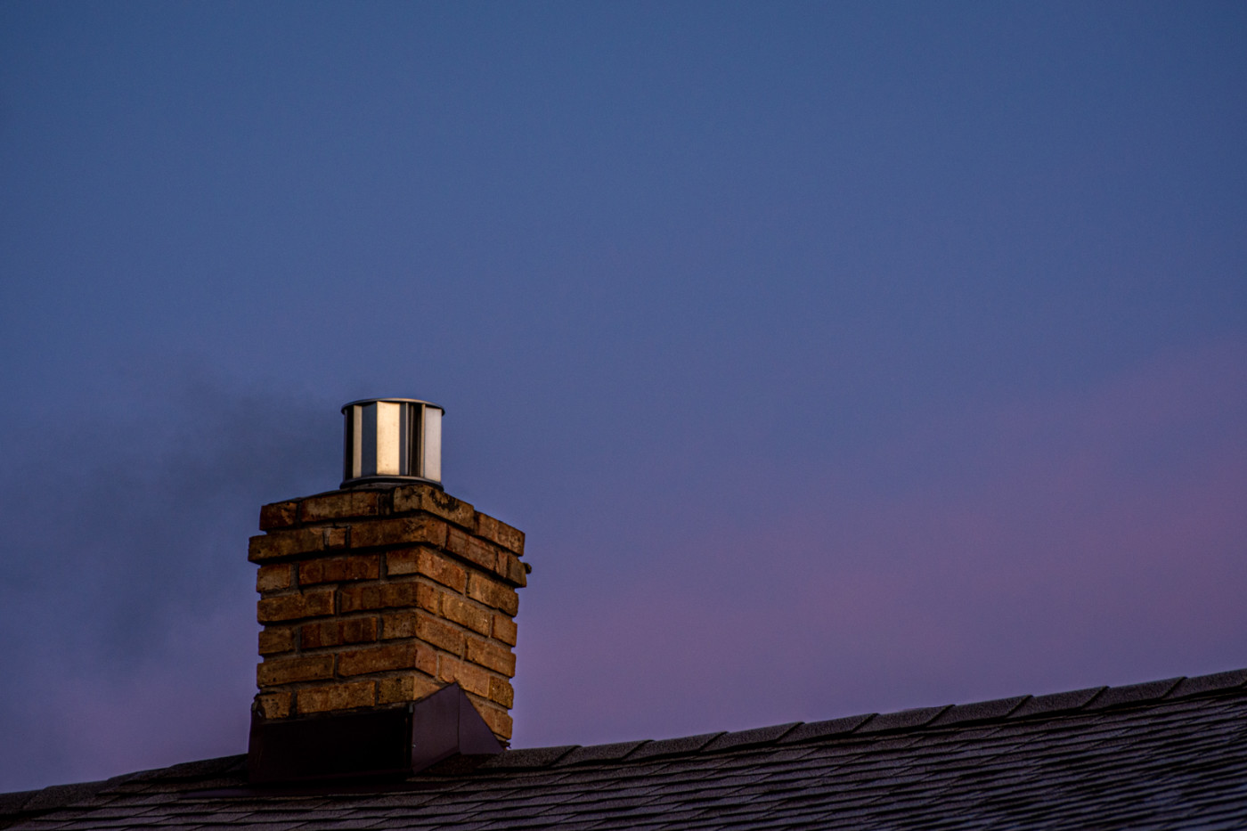 dark rooftop with brick chimney and shiny metal stack against a deep blue sky