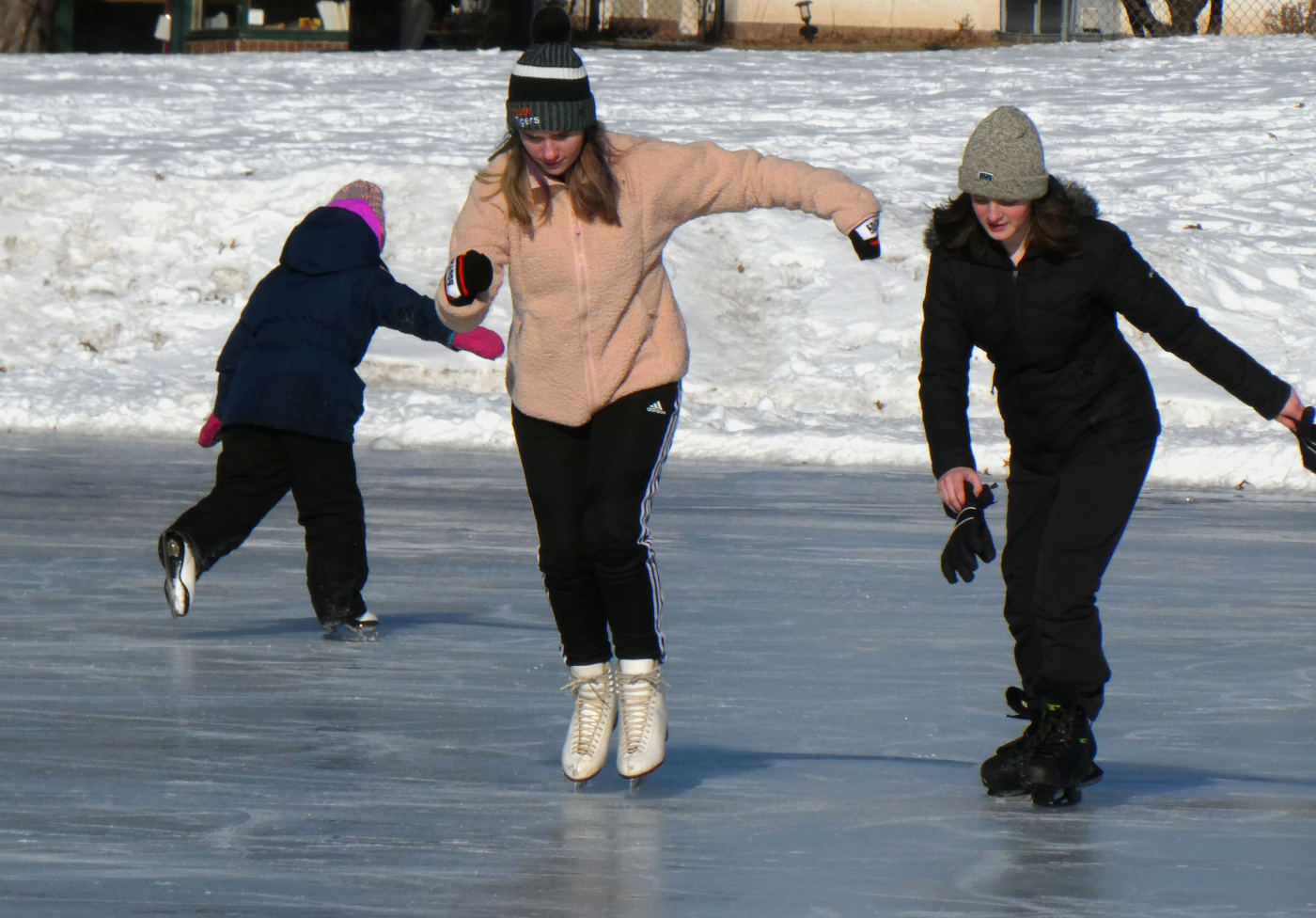 three young people ice skating, middle skater on toes