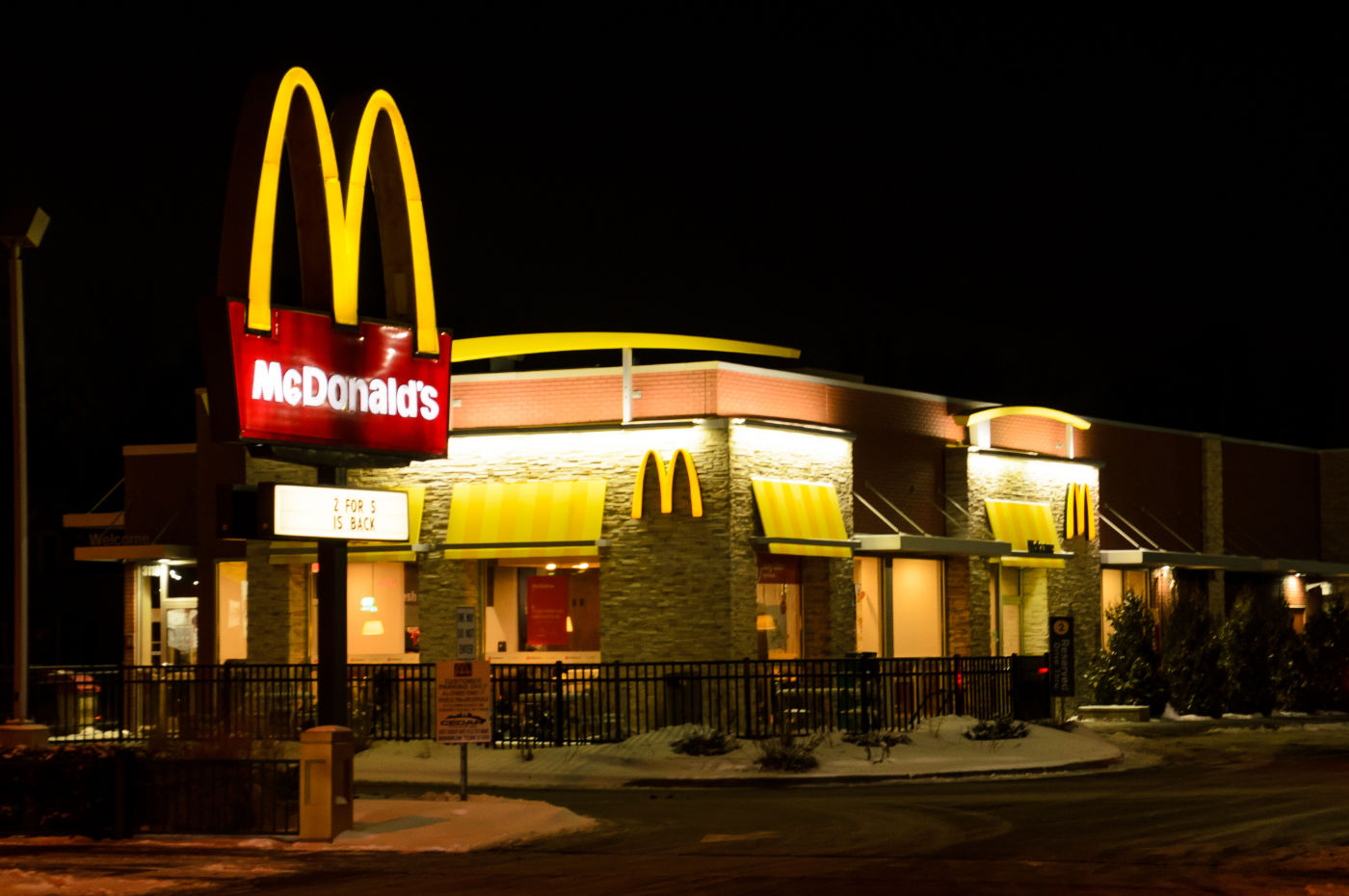 McDonald's restaurant outside at night with bright yellow lights and M-shaped arches atop red and white sign
