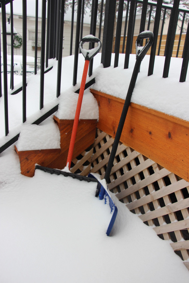 two snow shovels leaning against wood steps and porch covered in snow