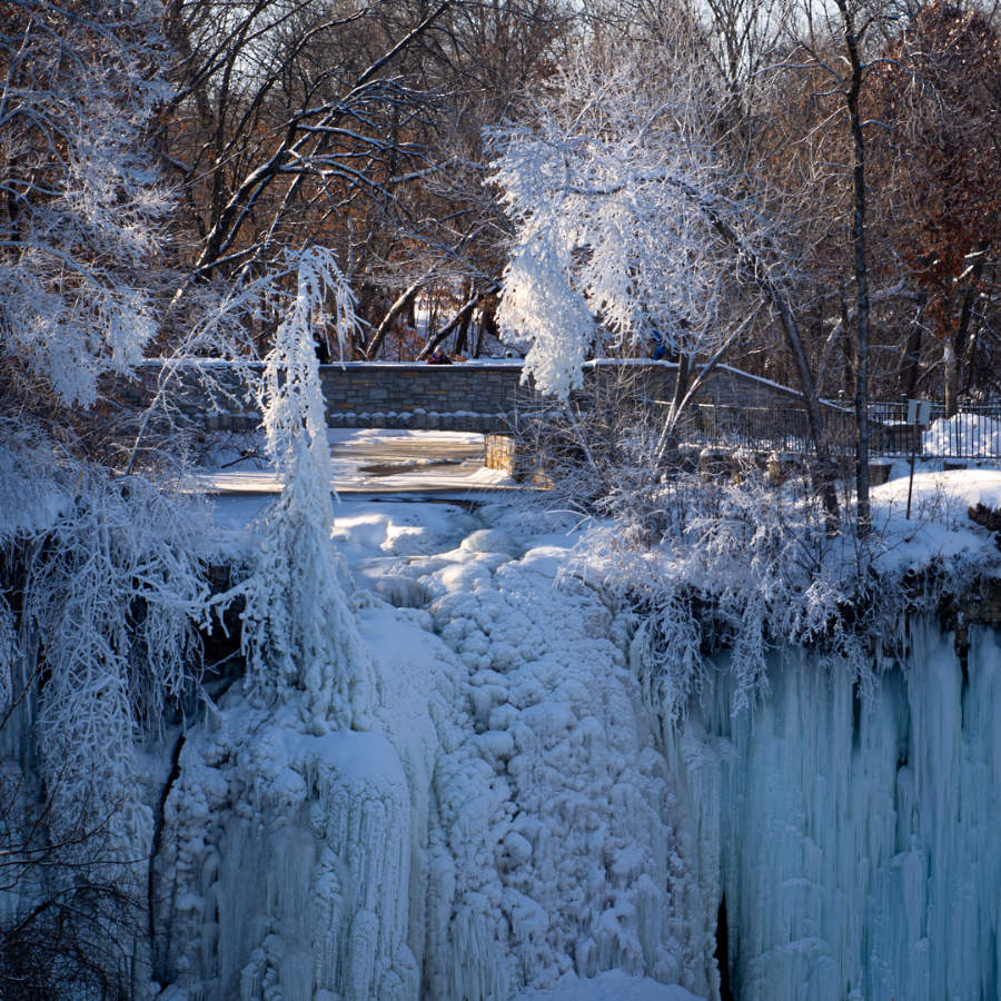 Frozen cascades and frosted tree limbs with a stone bridge above