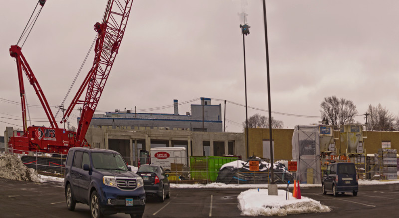 View of construction site with cars in a parking lot, low buildings, and a tall red construction crane