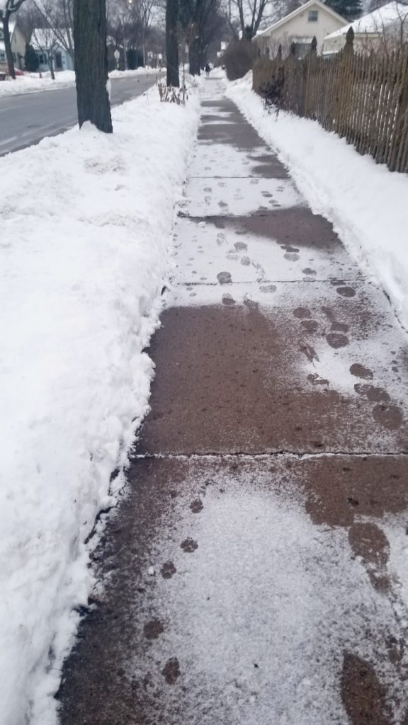 receding gray sidewalk dusted with snow and footprints in a winter urban landscape