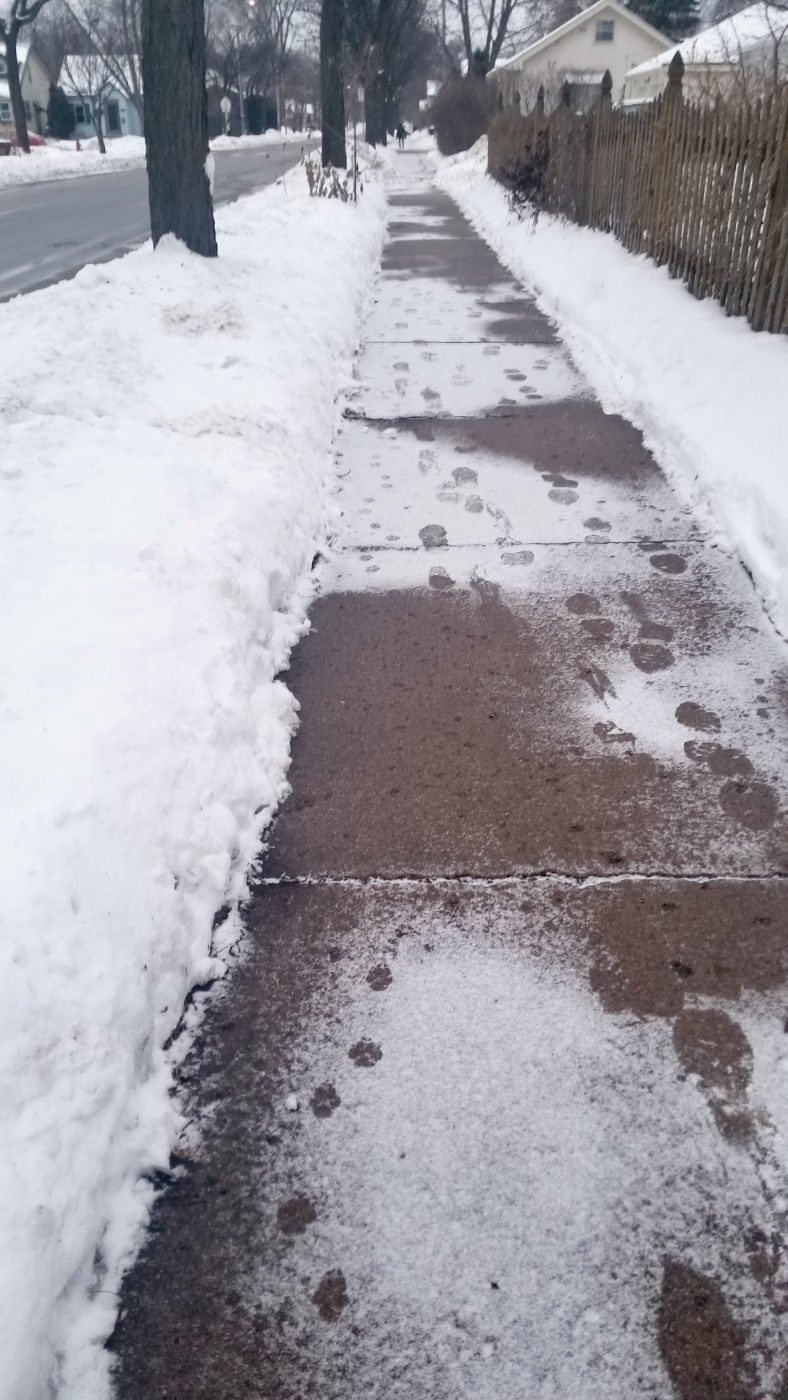 receding gray sidewalk dusted with snow and footprints in a winter urban landscape