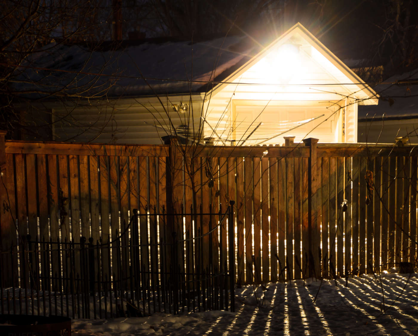 nighttime scene of a backlit wooden fence with a garage and overhead bright light in background