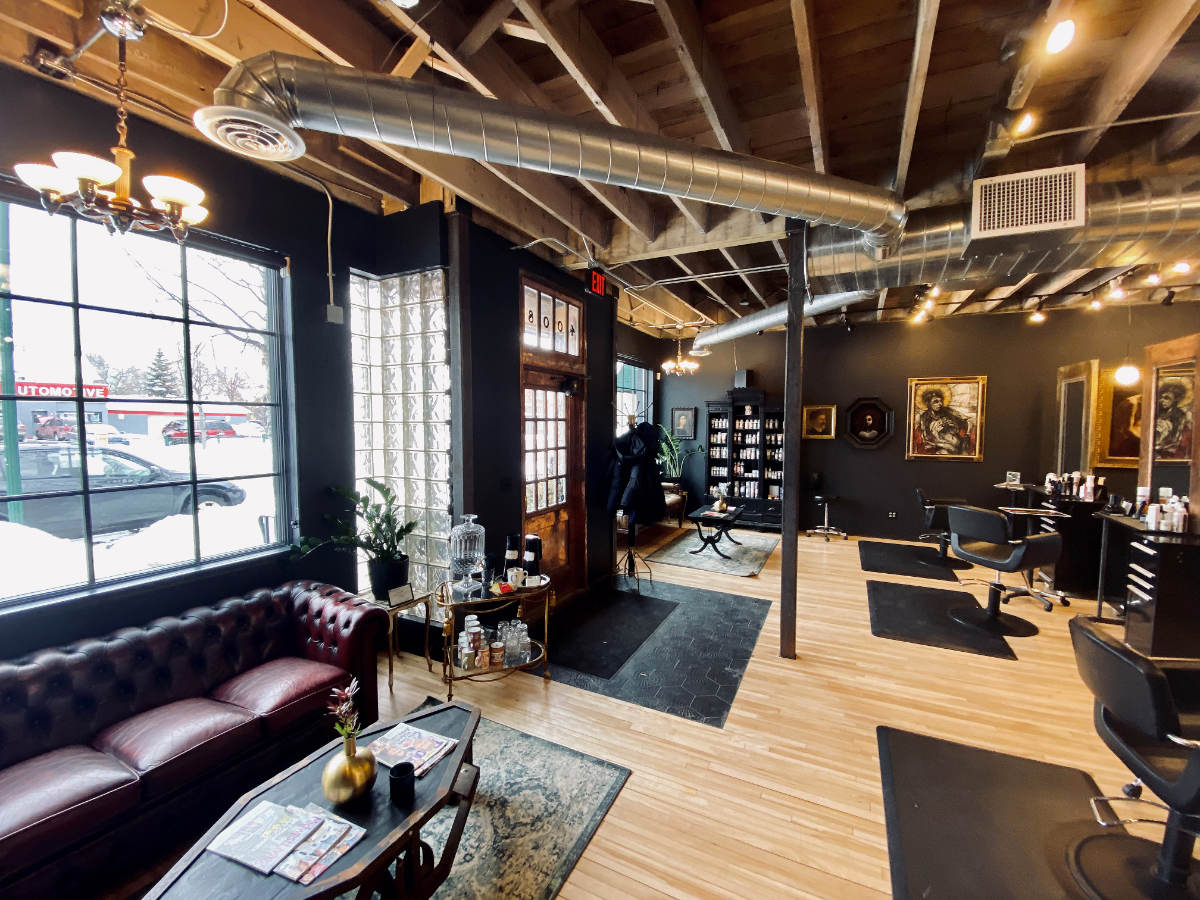 Retail lobby space in storefront with natural wood flooring and exposed ceiling beams, with black and brown furnishings, bright white light coming through windows and glass-block doorway