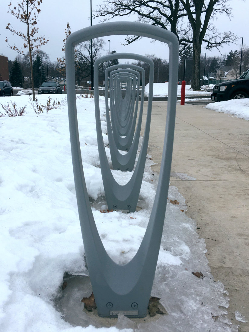 Receding row of curving triangular metal loops next to a sidewalk in winter on a gray day