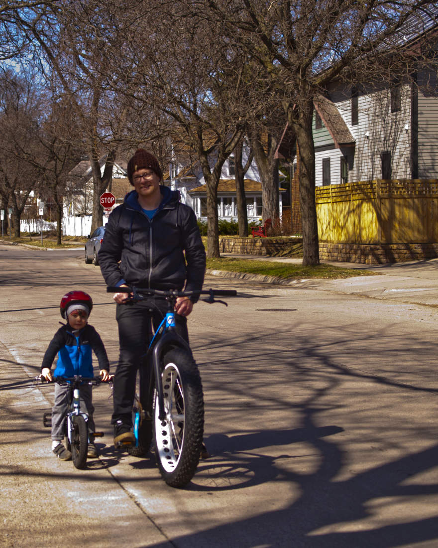 man and young boy on bicycles on a city street posed for the camera on a sunny day