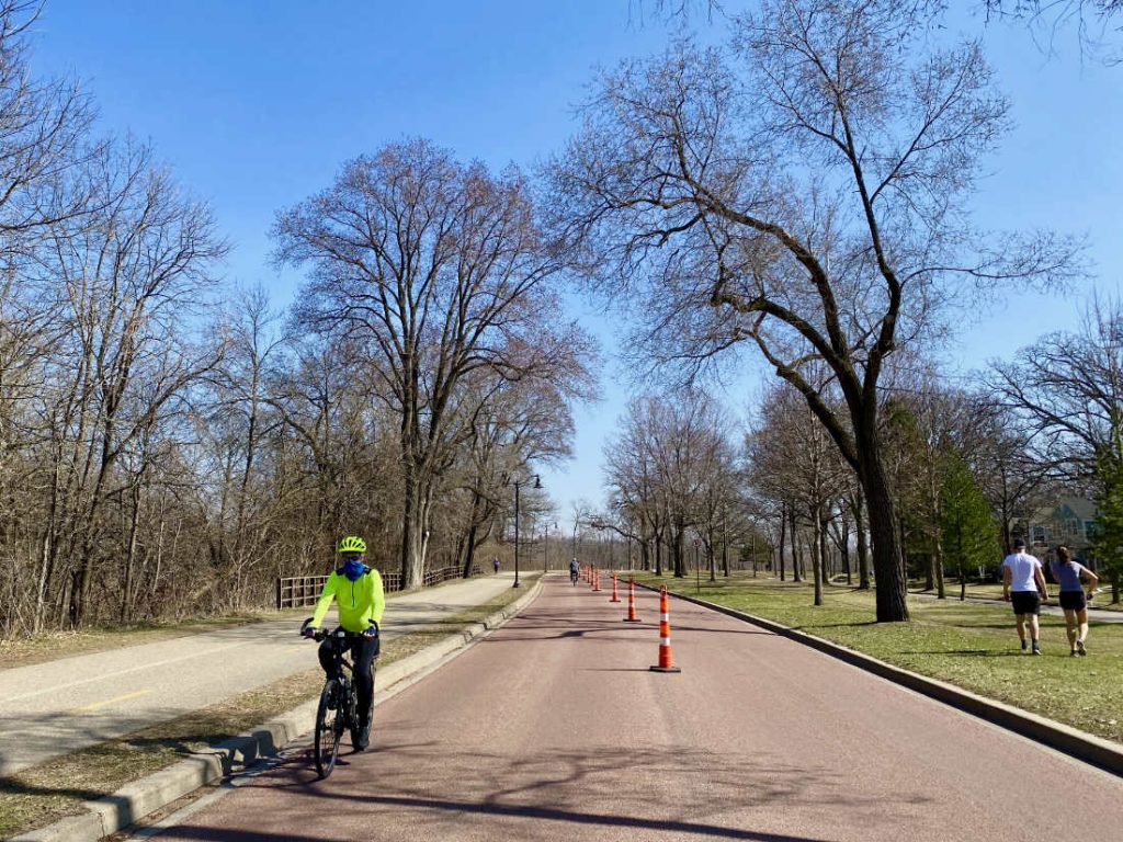 Bicyclist with fluorescent yell-green jacket and helmet on a parkway street with orange safety cones in the middle of the roadway