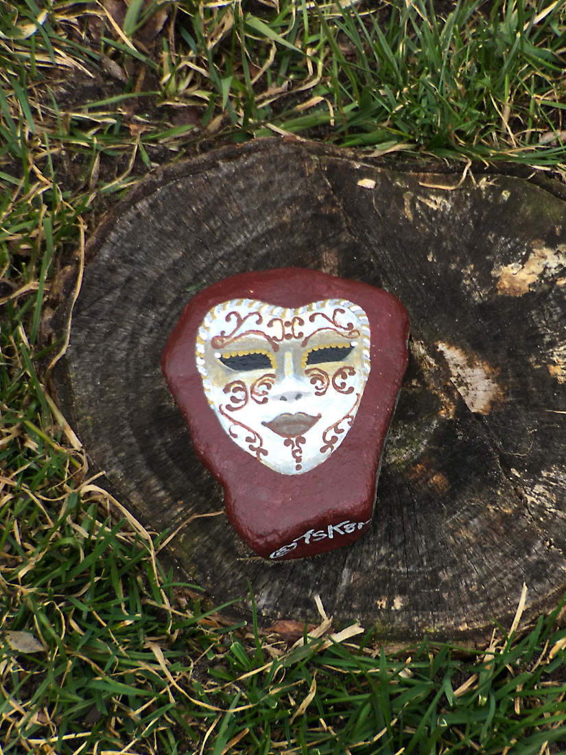 Painted artistic face design atop a tree stump in grass