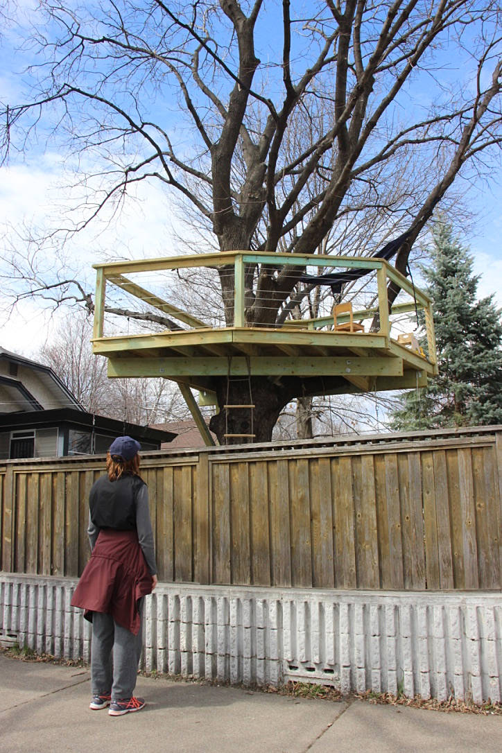 person from behind looking over a backyard wooden privacy fence up to a wooden treehouse platform