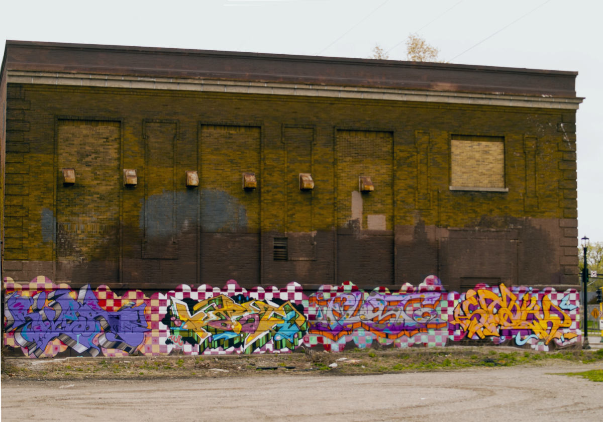 colorful arty graffiti with tags over checkerboard patterns along bottom panel of an old brown brick building