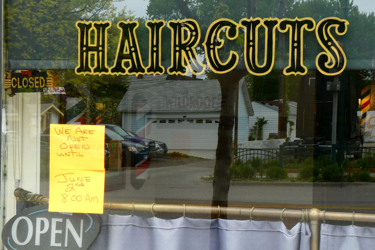Storefront window with painted sign for HAIRCUTS, with a note posted saying We are not open until June 2nd 8:00 am