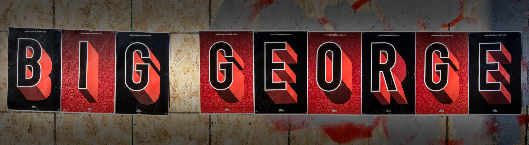 Sign hanging on plywood with red and black 3D letter blocks spelling "BIG GEORGE"