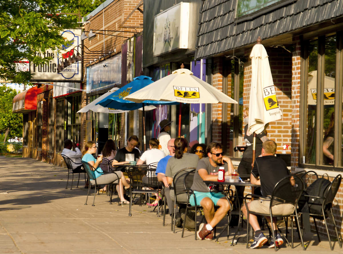 row of sidewalk cafe tables with diners in summer dress and sunglasses under table umbrellas