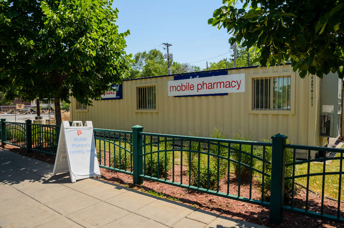 yellow mobile office unit sits behind an iron fence with a sign "mobile pharmacy" hanging on it