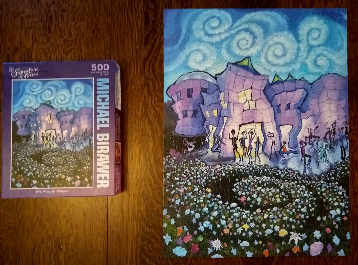 puzzle box on table next to a larger finished puzzle wit spiral garden, people dancing in front of purple building, with a sky of swirling clouds