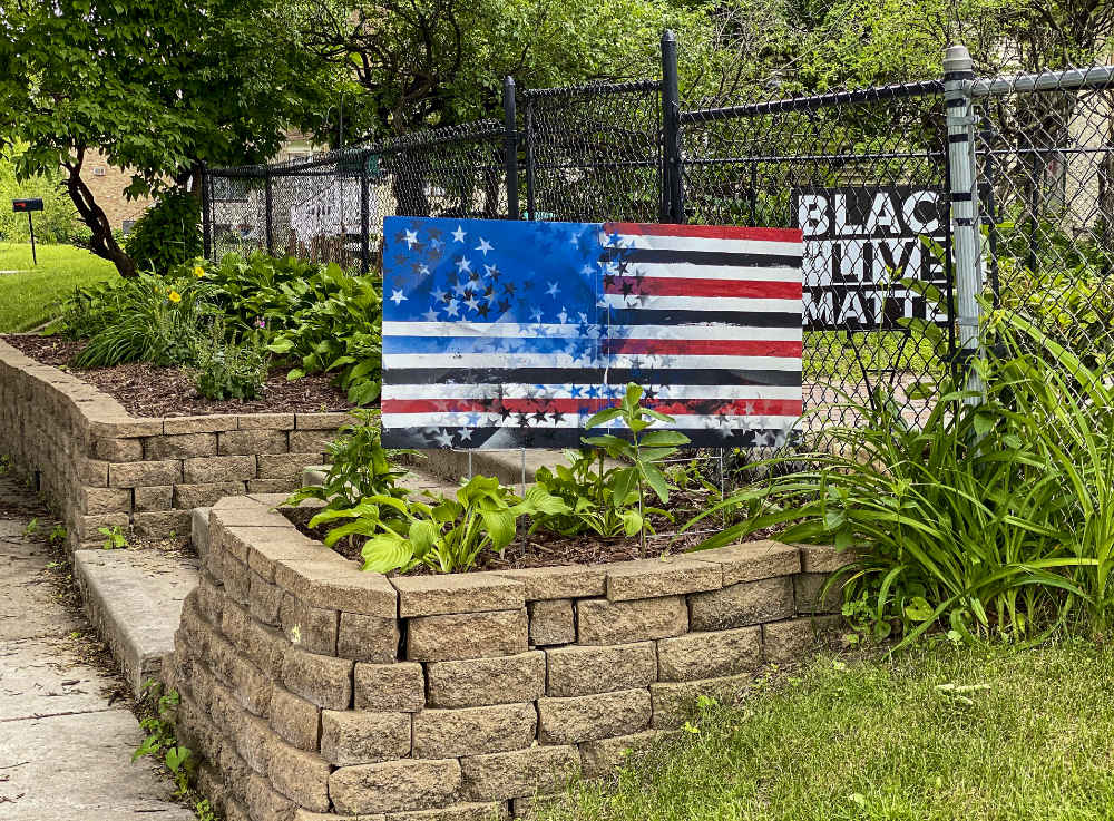 walled garden with an American flag art work (abstracted stars with red and white and black stripes) with a BLACK LIVES MATTER sign on a fence behind