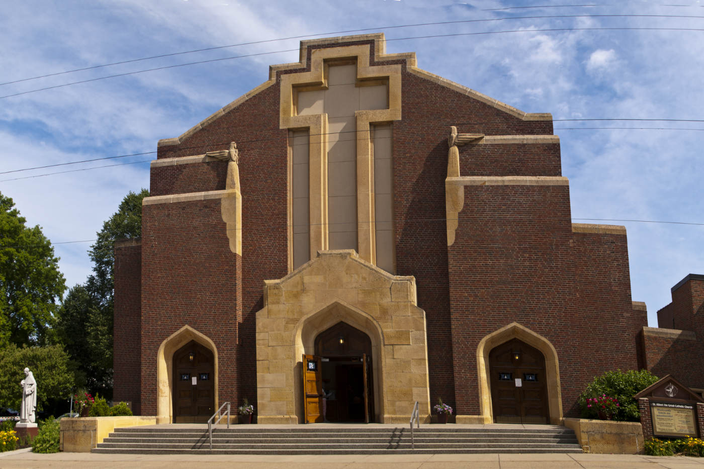 Front of red brick church building with yellow stone details and a large stone cross over the dooway