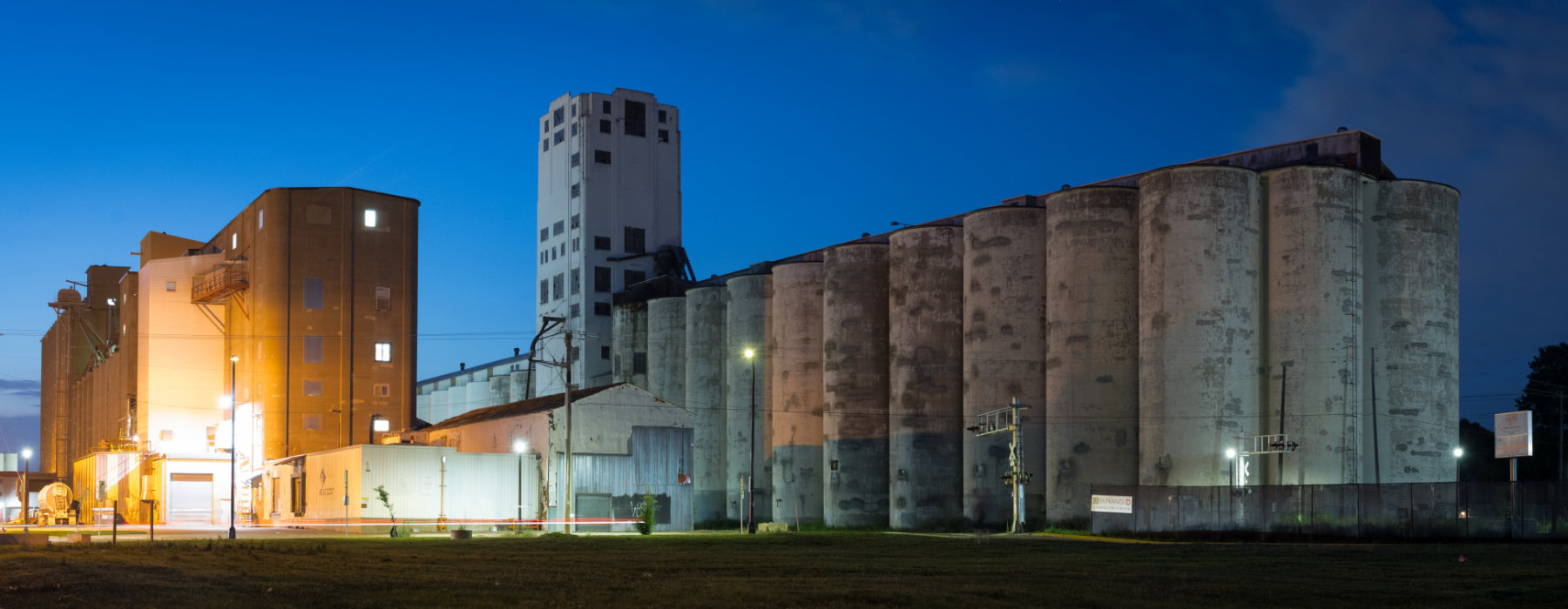 wide angle view of long row of grain elevators with a tall tower in the middle with deep blue sky