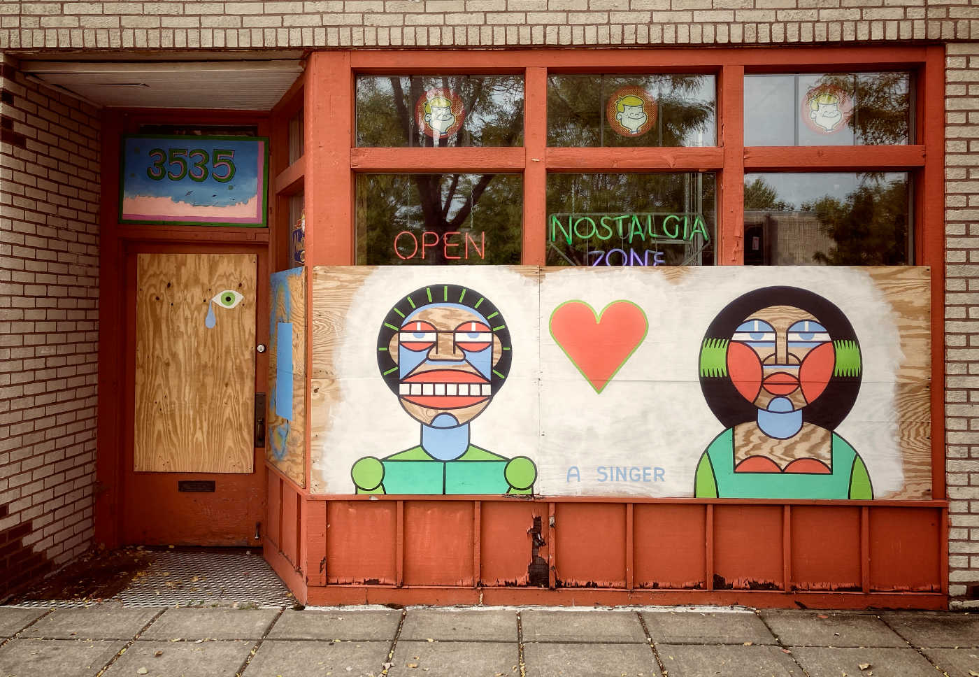 Storefront with partially boarded windows painted with a mural of cartoonish abstract figures and a red heart