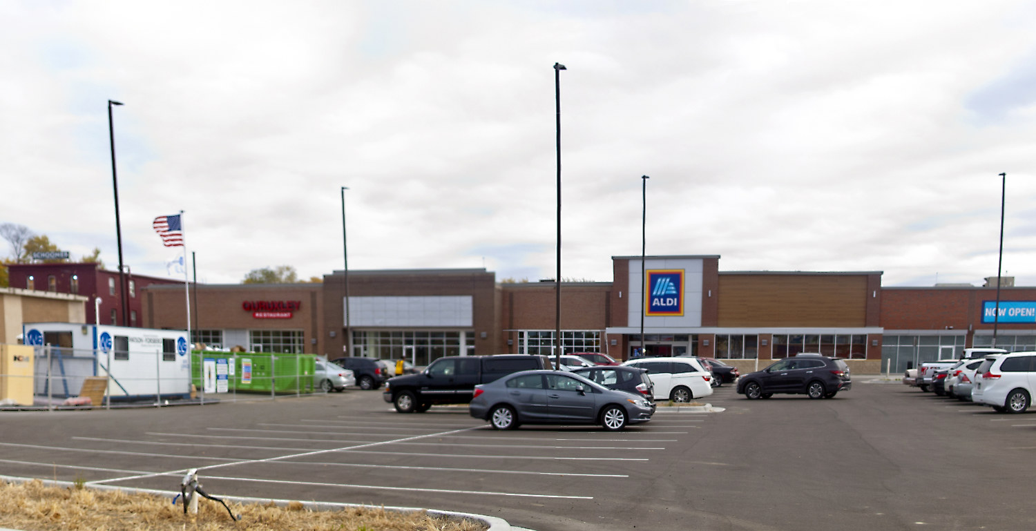 parking lot with some cars and an ALDI store with a Now Open sign on the building