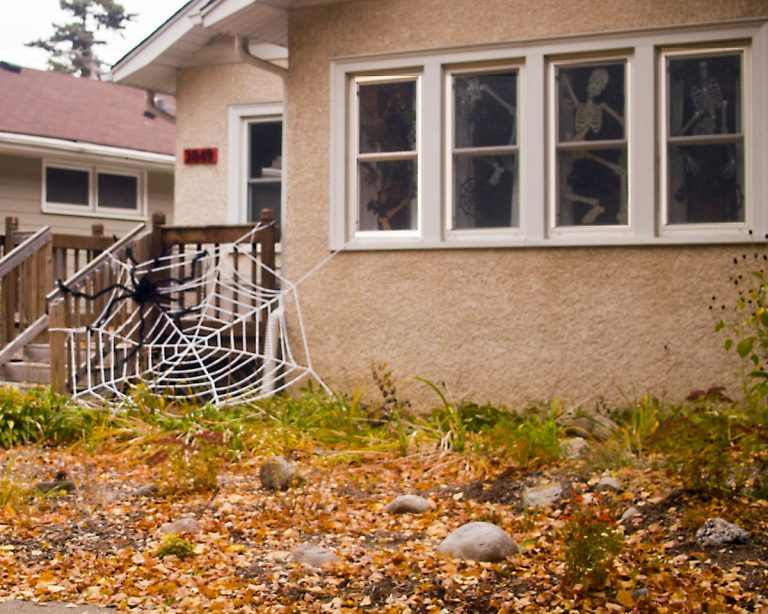 front yard of a house with a giant white rope spiderweb and black spider attached to the house and porch railing
