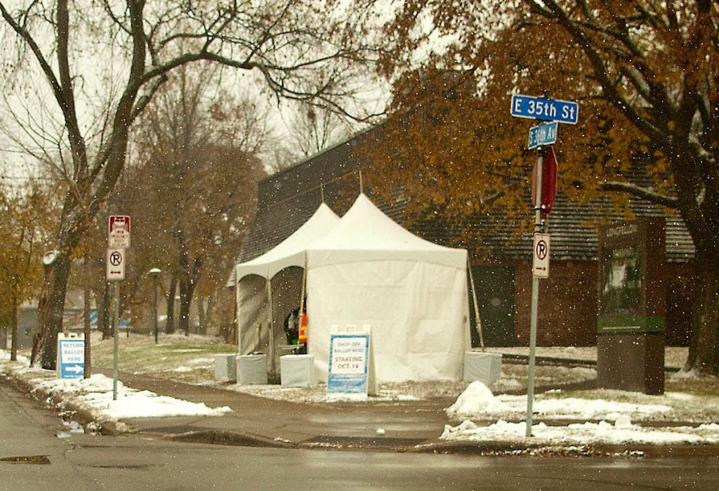 popup tent on street corner with Voting signs in light snow flurries