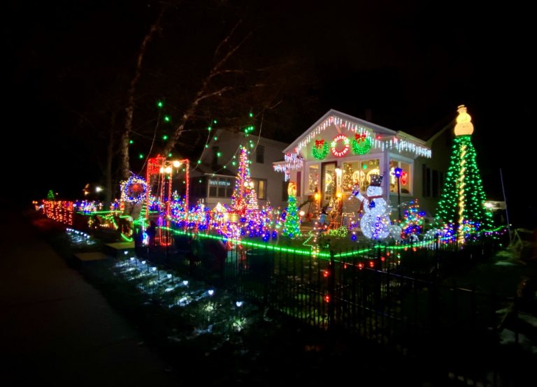 Fancifully colorful nighttime holiday decorations with lights on house and yard with trees, snowman and other displays