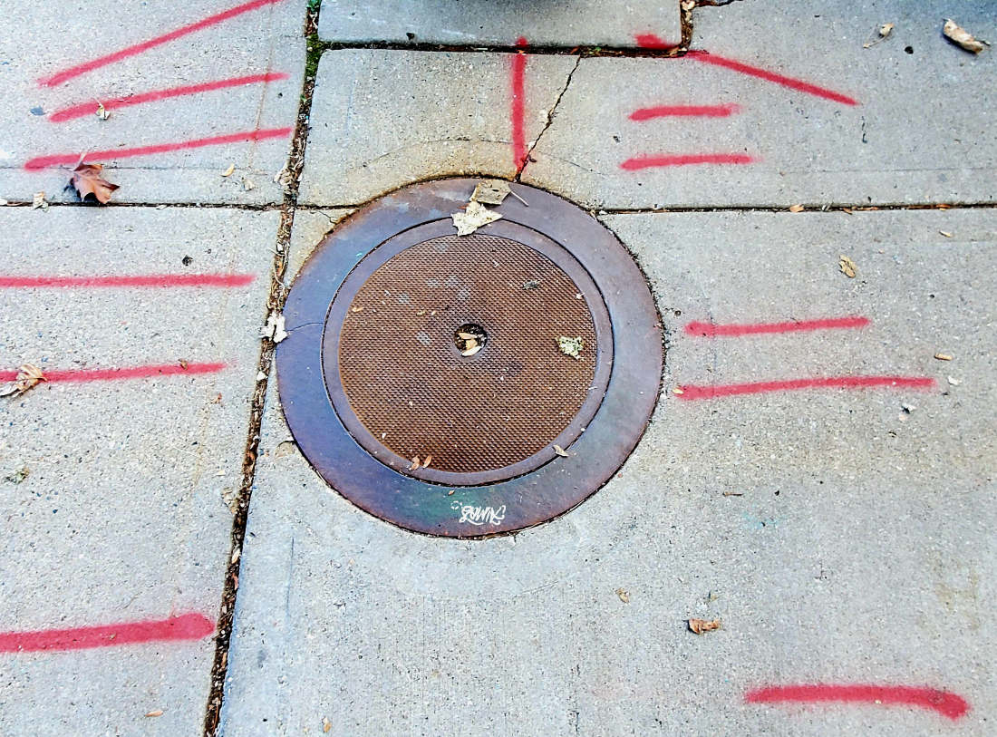 looking down at cement grid with rusty manhole cover surrounded by spray-painted red slashes