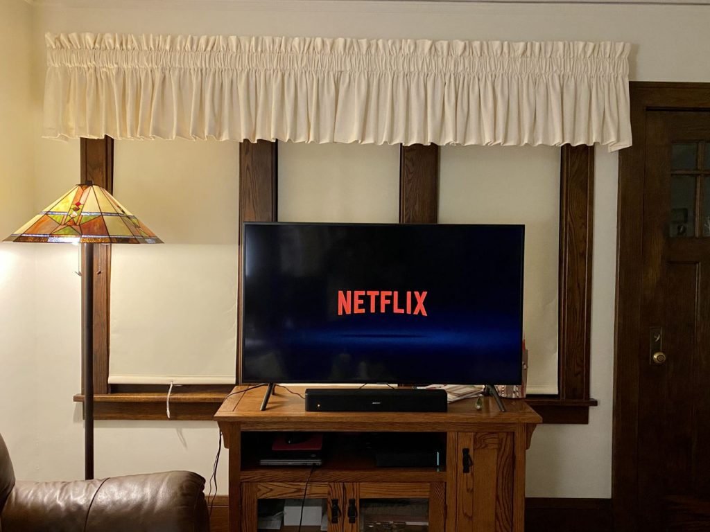 Television monitor on a wooden table in front of a window inside a house with the word NETFLIX on a black screen