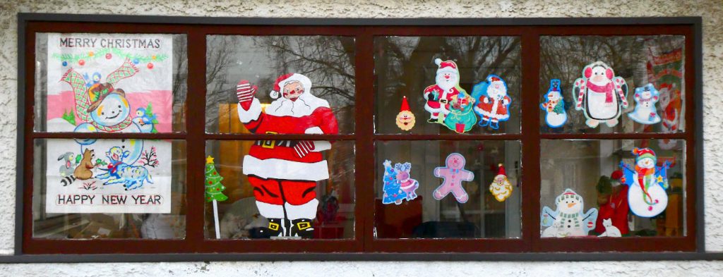 Four-paned window of house with a Santa picture and other holiday decorations hanging inside the windows