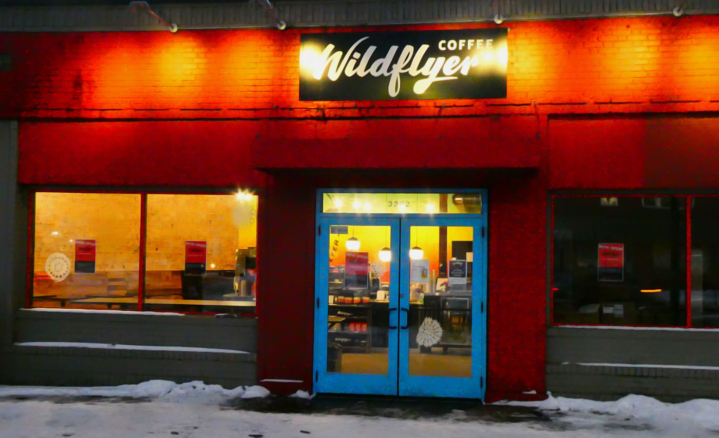 storefront door and windows at night with warm lighting inside and outside on overhead sign reading Wildflyer Coffee