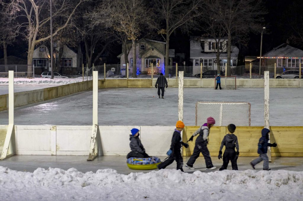 outdoor hockey rink at night with a group of children pulling one sitting on a inflated sliding tube