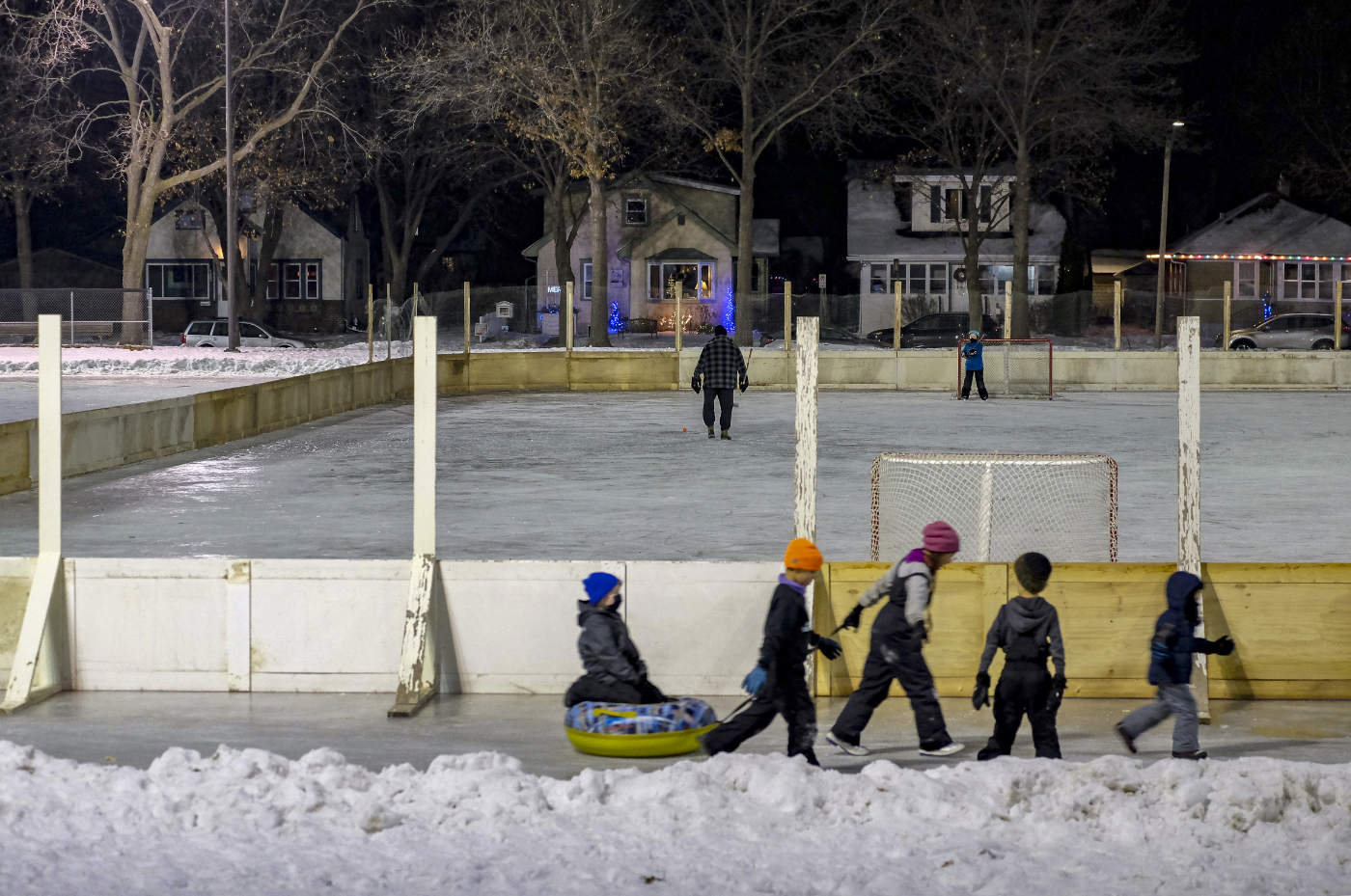 outdoor hockey rink at night with a group of children pulling one sitting on a inflated sliding tube