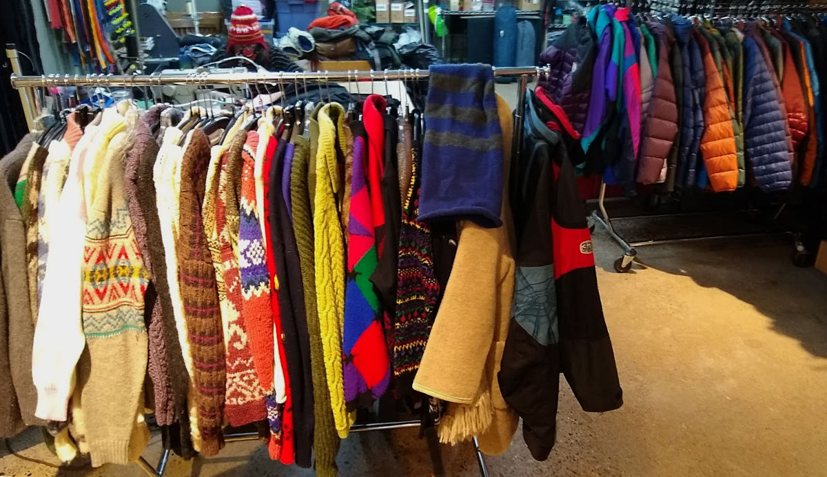Brightly colored winter sweaters hang tightly together on a close rack in a store with more colors and garments in background