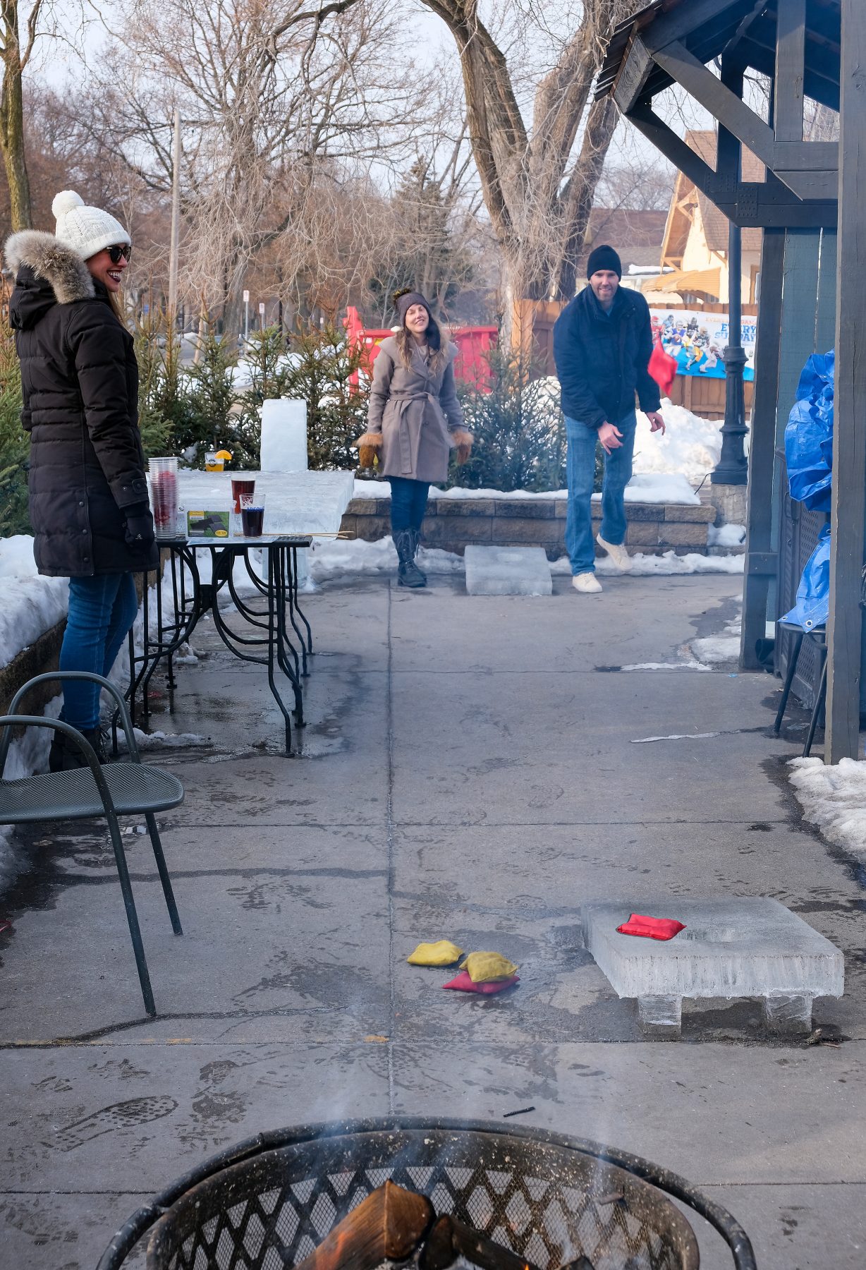 People outside in winter garb playing bean bag toss on a cement patio