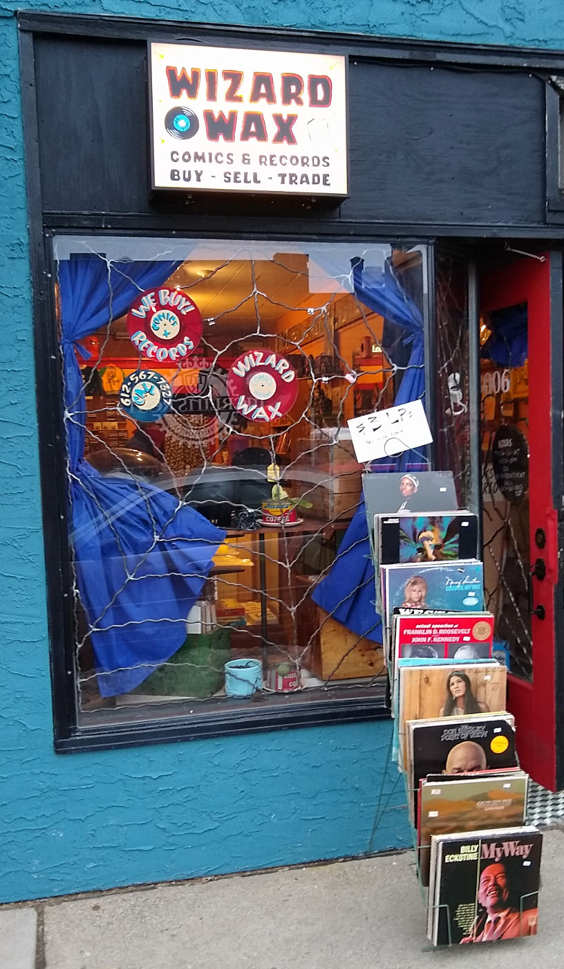 rack of records on sidewalk in front of a colorful storefront window with Wizard of Wax sign overhead