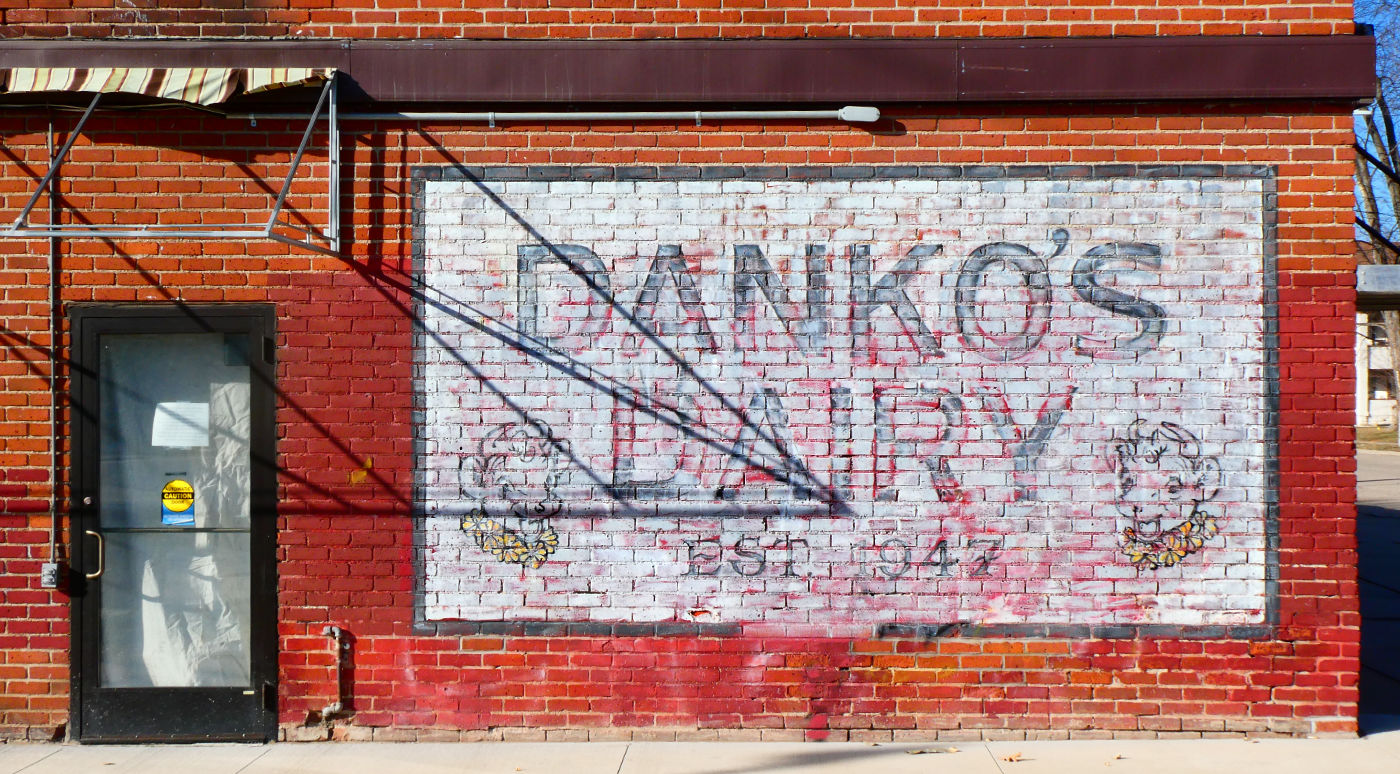faded sign on a red brick wall reading DANKO'S DAIRY with cartoonish cow heads