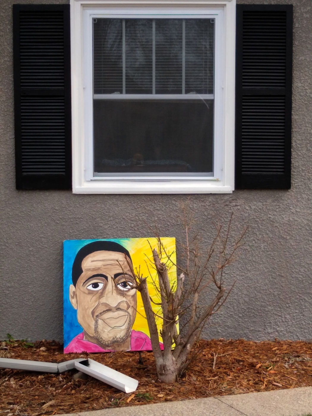 colorful painted portrait of a black man on canvas resting against a brown stucco wall with black and white window