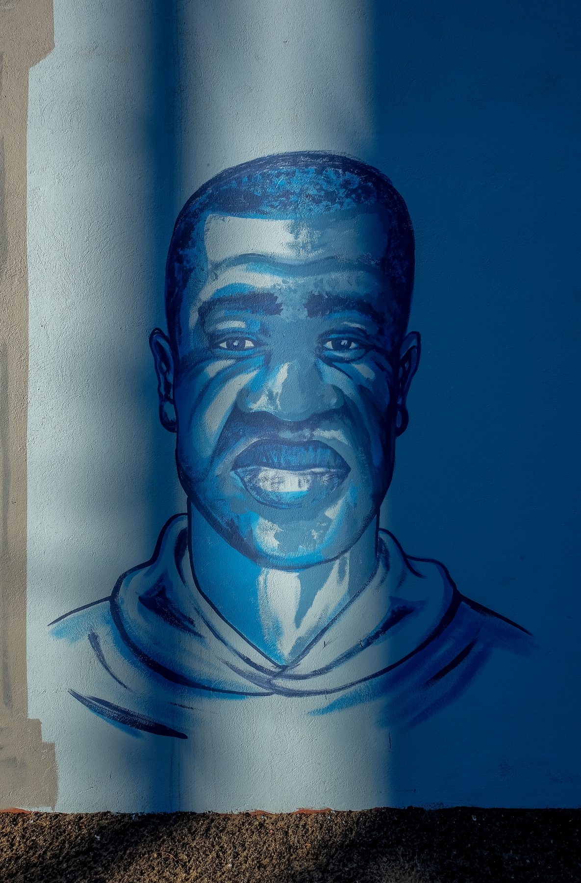 Sunlight illuminates a beautifully painted mural of George Floyd. The paint colors... all shades of blue.