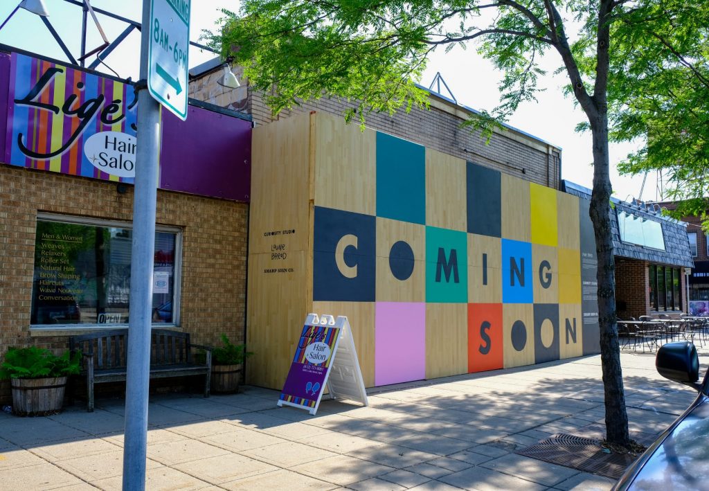 A decorative display on plywood indicates three businesses are Coming Soon
